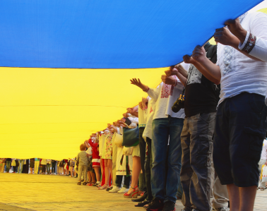 Ukrainians hold a vast flag at a patriotic ceremony.