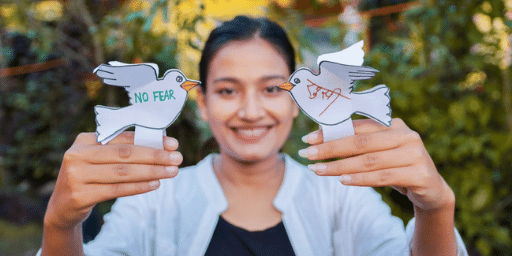 Young woman with dark hair and light brown skin holds her hands out with a paper dove resting on each finger